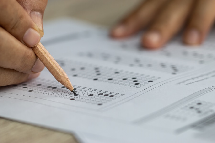 School Students hands taking exams, writing examination holding pencil on optical form of standardized test, by By smolaw11.